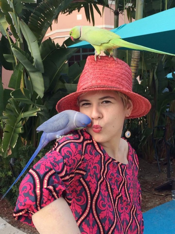 Paula Rosenberg with two parakeets perched on her hat and shoulder